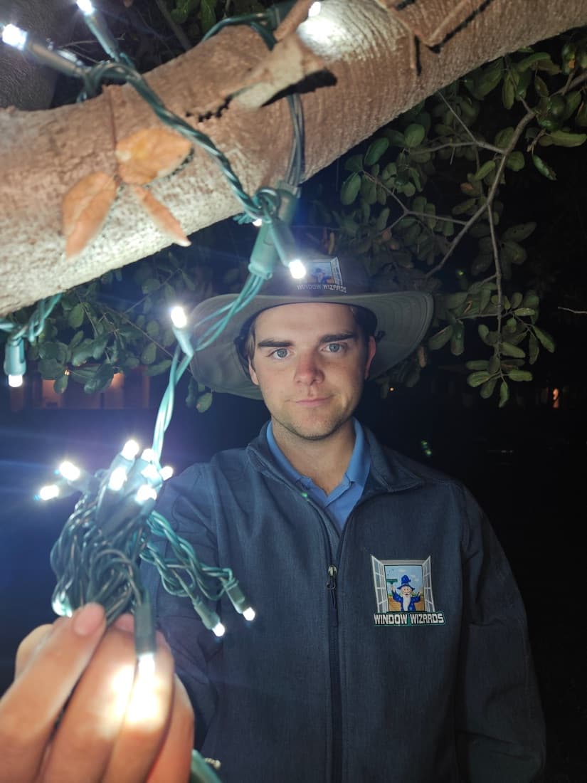 Will Downing, owner of Window Wizards, hanging holiday lights in Window Wizards gear