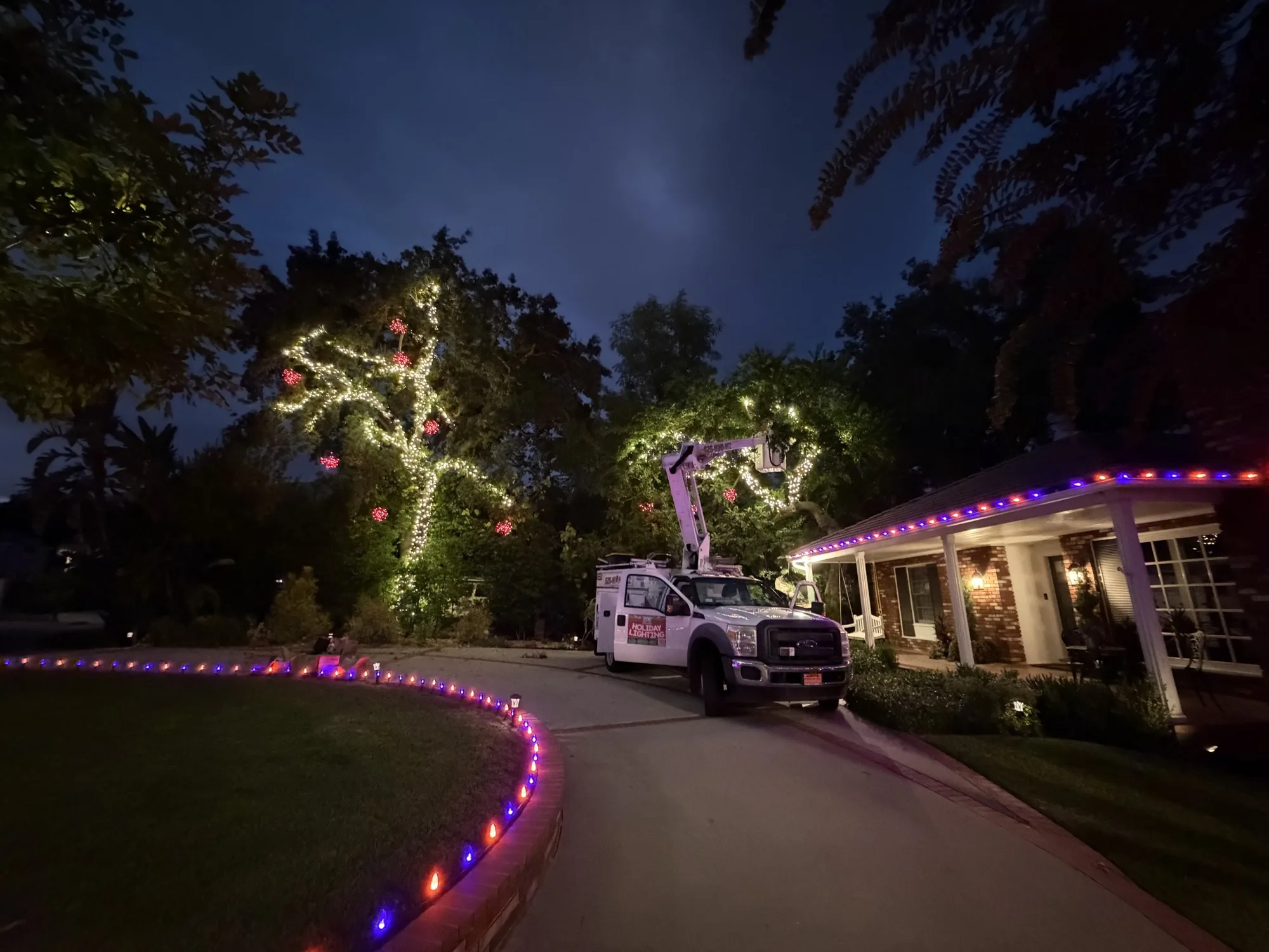 626 Christmas bucket truck on-site installing roofline lights and a wrapped tree