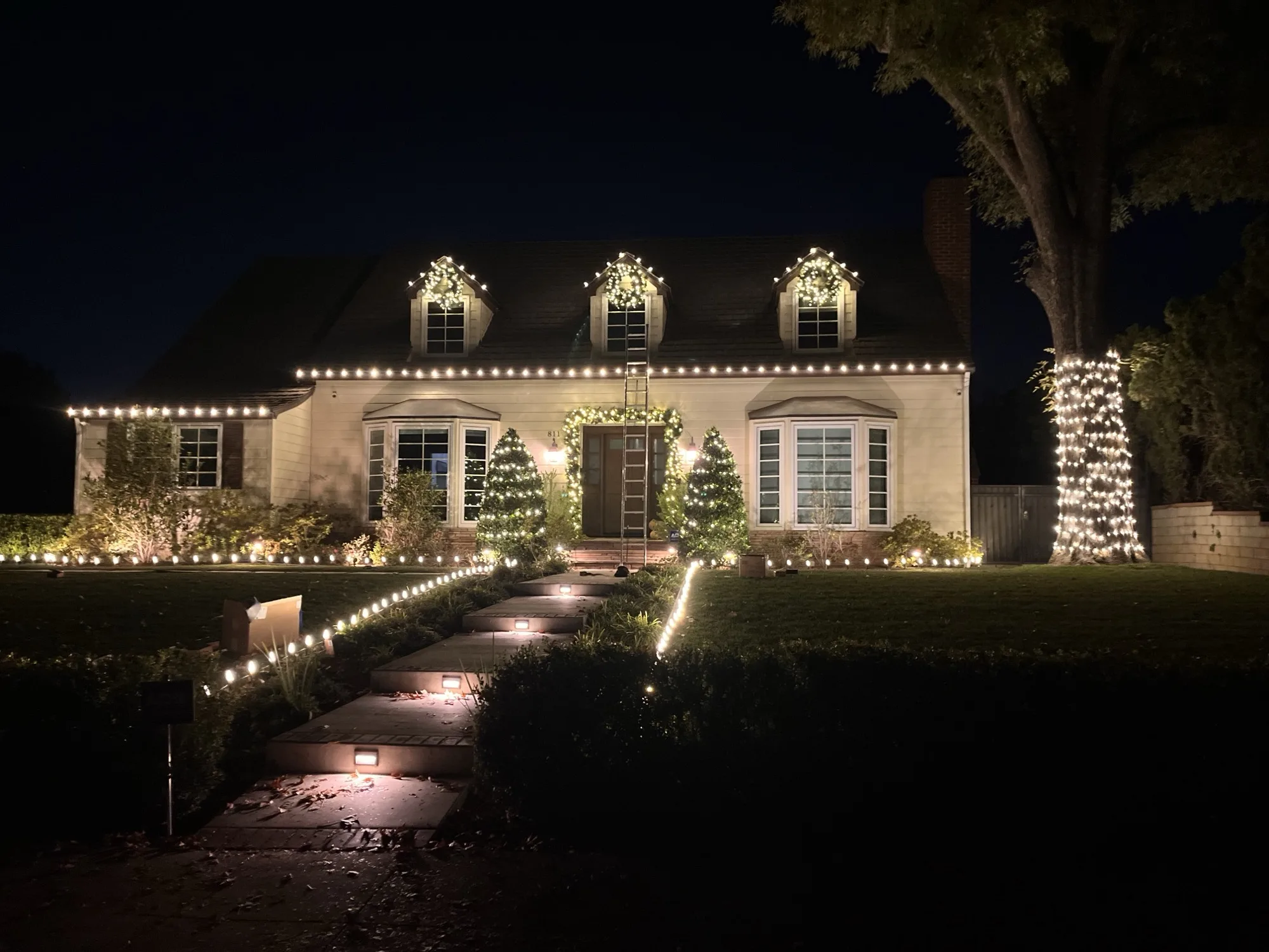 Cape Cod home with warm-white roofline lights and dormer wreaths by 626 Christmas