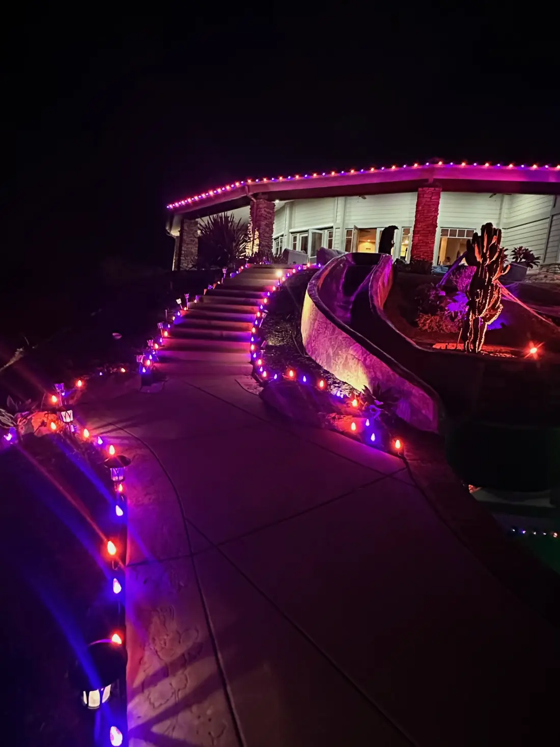 Purple and orange pathway lighting running up stone steps to a hillside home at night