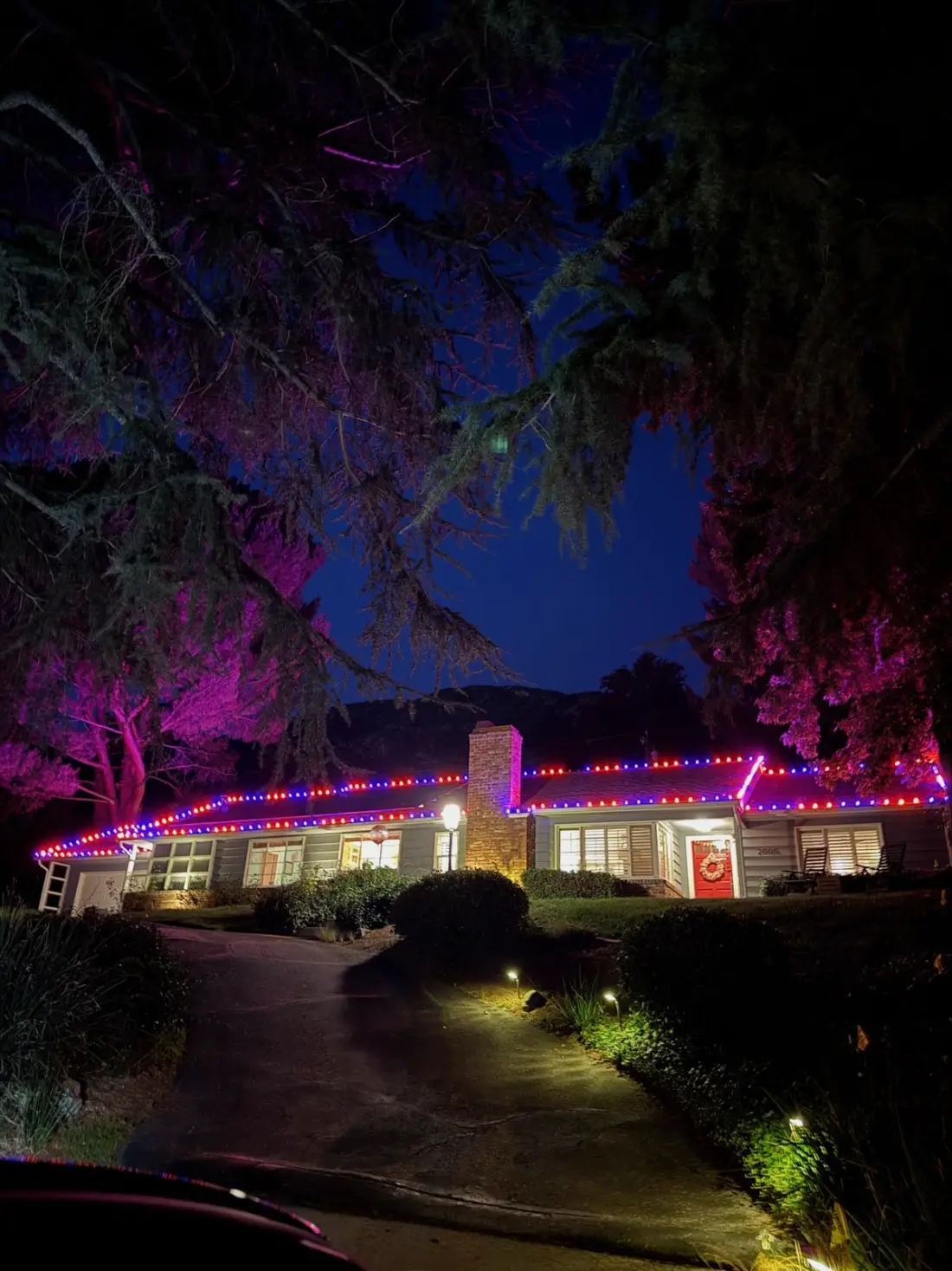 Ranch home roofline outlined in orange and purple Halloween lights under mature trees